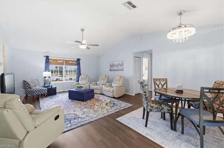 Open-concept living area featuring wood-finish flooring, vaulted ceilings, and a large window with horizontal blinds