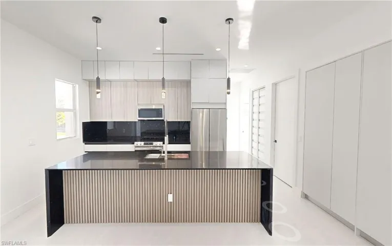 Kitchen with modern cabinets, stainless steel appliances, dark countertops, a sink, and pendant lighting