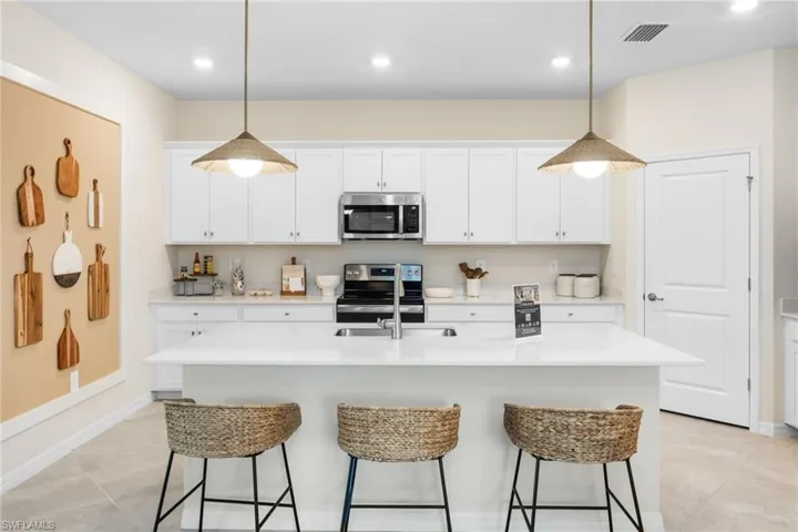 White cabinetry, stainless steel appliances, central island with seating, pendant lighting, and light-toned flooring