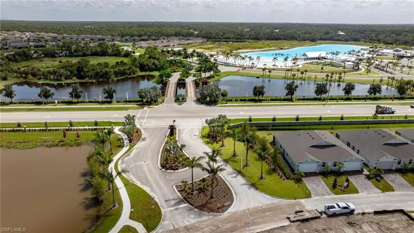Community entrance featuring paved roads, manicured landscaping, and proximity to a large recreational lagoon
