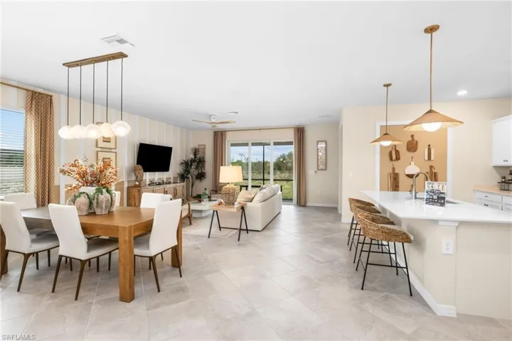Spacious open-concept living area featuring a dining space with a linear pendant light fixture, a kitchen island with pendant lighting, and light-toned tile flooring throughout