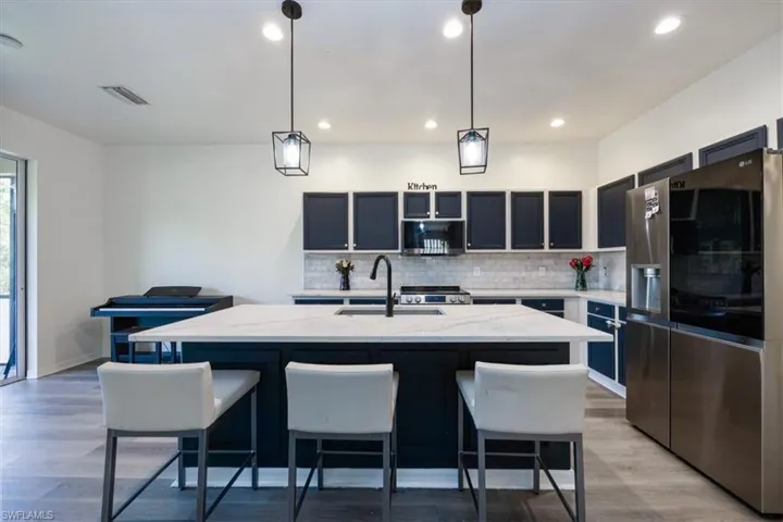 Kitchen with stainless steel appliances, backsplash, pendant lighting, a center island with sink, and a kitchen breakfast bar