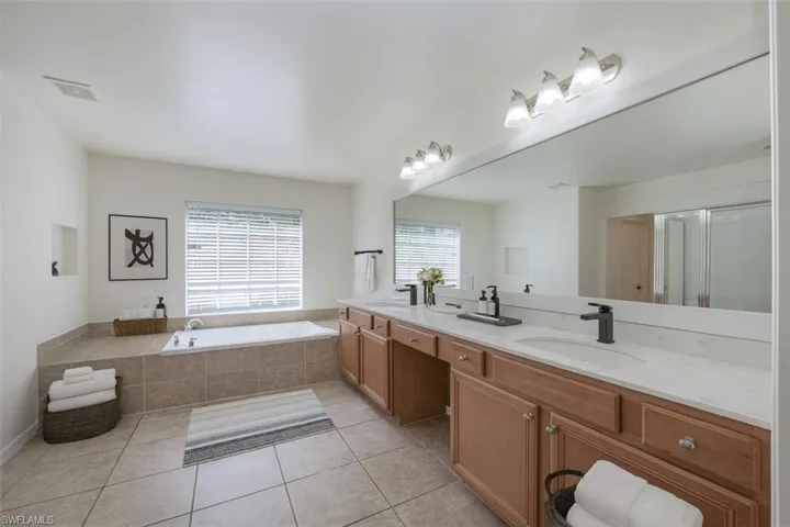 Full bathroom with double vanity, light tile patterned floors, a garden tub, and a shower with shower door