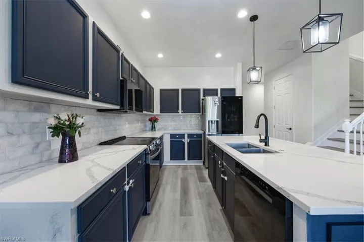 Kitchen with backsplash, black appliances, hanging light fixtures, light stone countertops, and recessed lighting