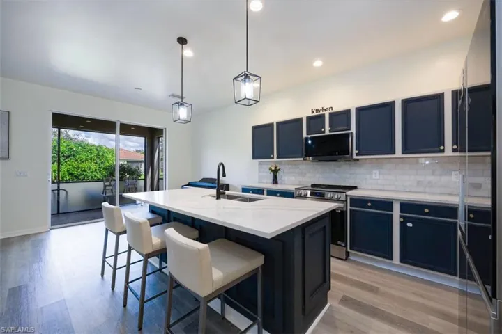 Kitchen featuring decorative backsplash, decorative light fixtures, dark cabinetry, stainless steel electric range, and an island with sink