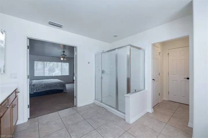 Ensuite bathroom with vanity, light tile patterned flooring, a stall shower, and ceiling fan