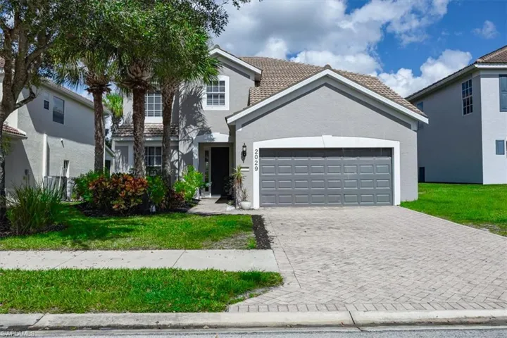 Traditional home featuring decorative driveway, an attached garage, stucco siding, and a front lawn
