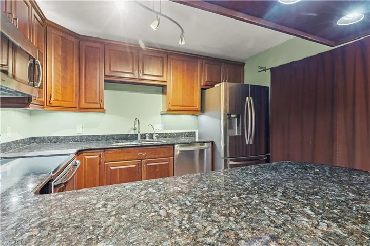 Kitchen with dark stone counters, stainless steel appliances, and brown cabinetry