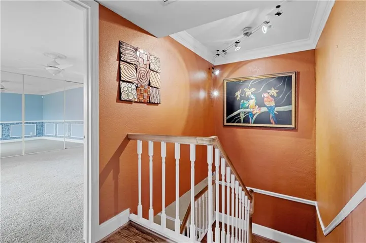Stairway with crown molding, a textured wall, carpet floors, track lighting, and a ceiling fan