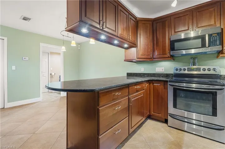 Kitchen featuring appliances with stainless steel finishes, a peninsula, light tile patterned flooring, and dark stone countertops