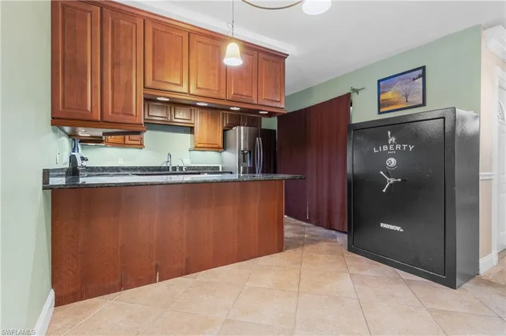 Kitchen with a peninsula, brown cabinetry, dark stone counters, stainless steel fridge, and decorative light fixtures