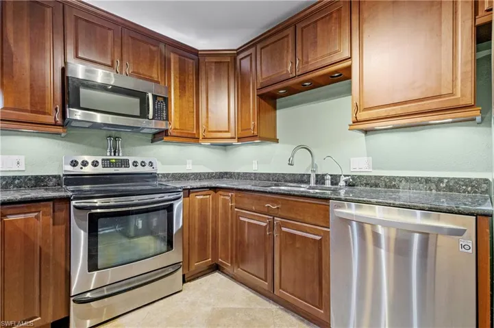 Kitchen with appliances with stainless steel finishes, dark stone countertops, and brown cabinets