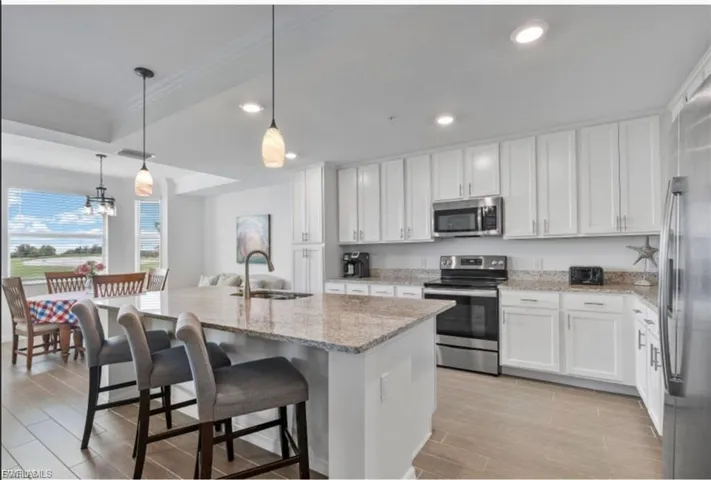 Kitchen featuring stainless steel appliances, decorative light fixtures, white cabinets, a breakfast bar, and light stone countertops