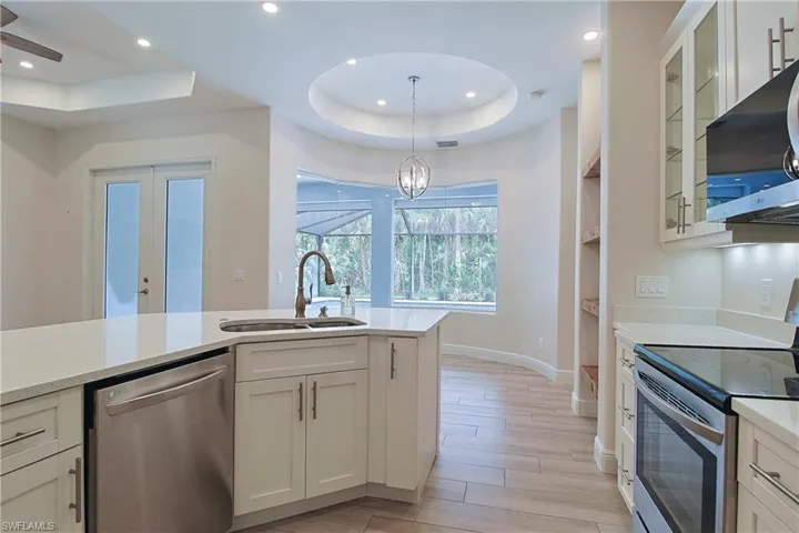 Modern kitchen featuring light cabinetry, stainless steel appliances, quartz countertops, a kitchen island with sink, and wood-finish flooring