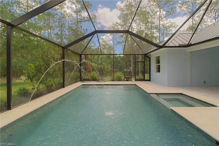 Screened lanai featuring a swimming pool with water features, an integrated spa, and light-colored deck pavers