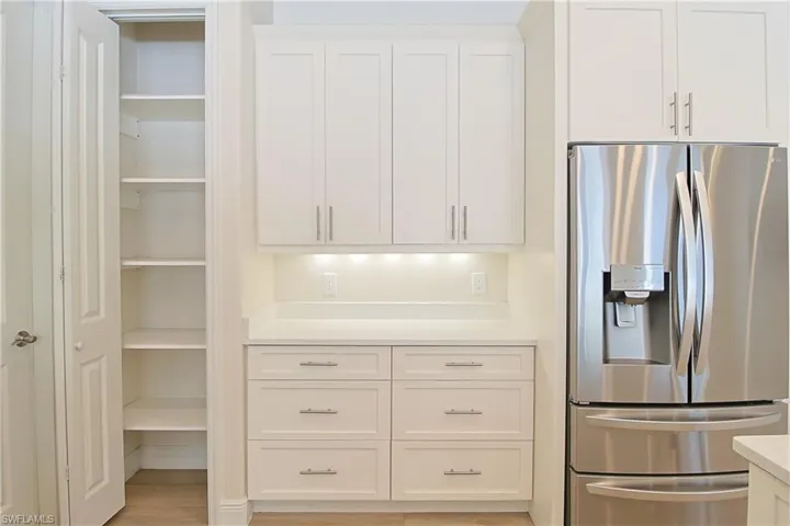 White shaker-style cabinetry with brushed nickel hardware, built-in shelving, under-cabinet lighting, and stainless steel French door refrigerator