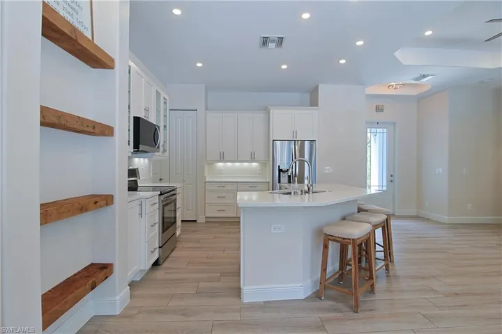 Modern kitchen featuring white cabinetry, stainless steel appliances, a center island with bar seating, wood-finish flooring, and recessed lighting