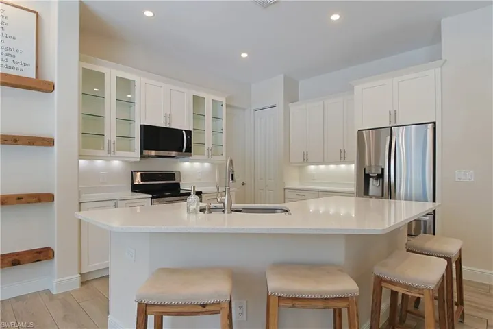 Modern kitchen featuring white cabinetry, stainless steel appliances, a white solid surface island with an undermount sink, and recessed lighting
