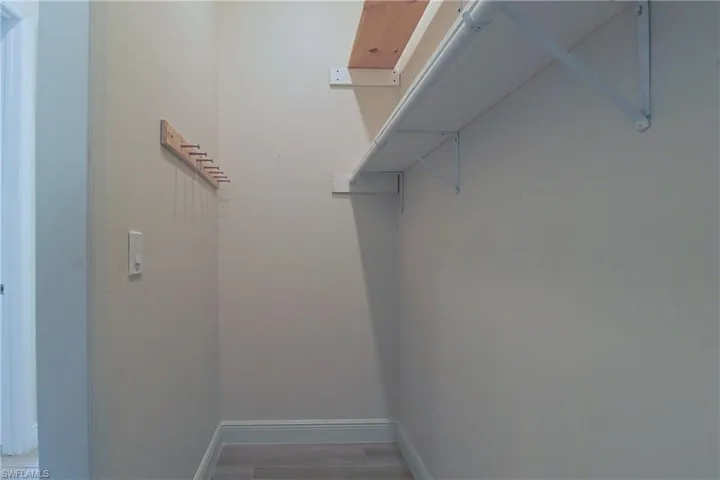Interior closet space featuring light-toned walls, a wood-finish flooring, white baseboards, a wall-mounted coat rack, and white shelving with a hanging rod