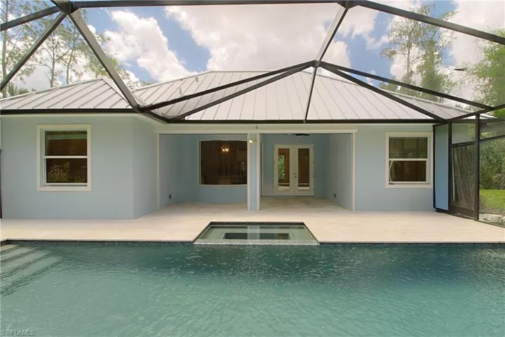 Screened enclosure featuring a swimming pool with integrated spa, light blue exterior siding, white metal roof, and an expansive patio