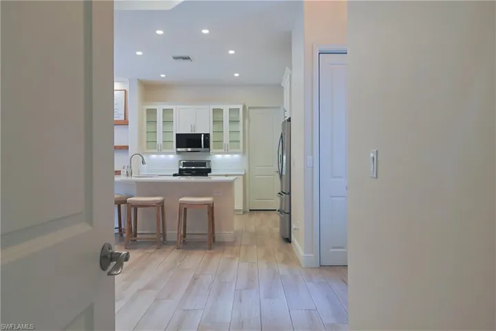Bright kitchen featuring recessed lighting, white cabinetry with glass inserts, stainless steel appliances, a white tile backsplash, and an island with bar seating