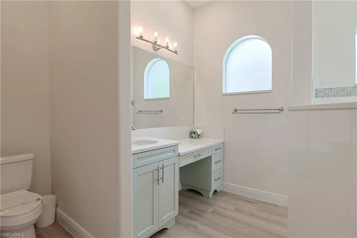 Bathroom featuring wood-finish flooring, a light green vanity with integrated sink and countertop, and a separate dressing vanity