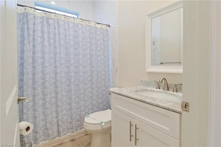 Bathroom vanity featuring a marble countertop with an integrated sink, brushed nickel faucet, and white framed mirror