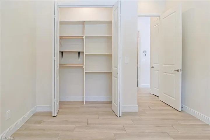 Room with wood-finish flooring and a bi-fold closet featuring built-in shelving and a clothing rod