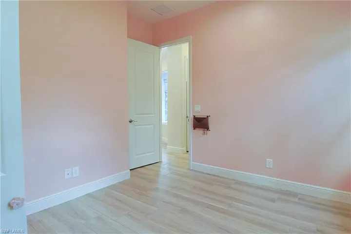 Room featuring wood-finish flooring, light pink walls, and white baseboards