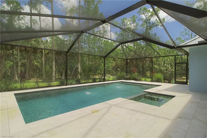 Screened pool enclosure with a rectangular pool, integrated spa, light-colored paver decking, and a backdrop of mature trees
