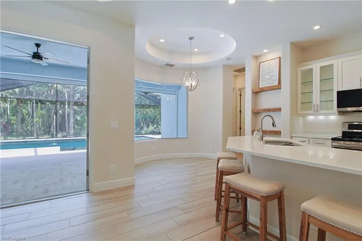 Open-concept kitchen and dining area featuring a breakfast bar with seating, light-toned wood-finish flooring, and a large sliding glass door opening to a screened patio with a pool
