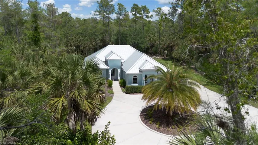 Light blue exterior with a white metal roof, featuring a circular driveway, mature palm trees, and lush surrounding foliage