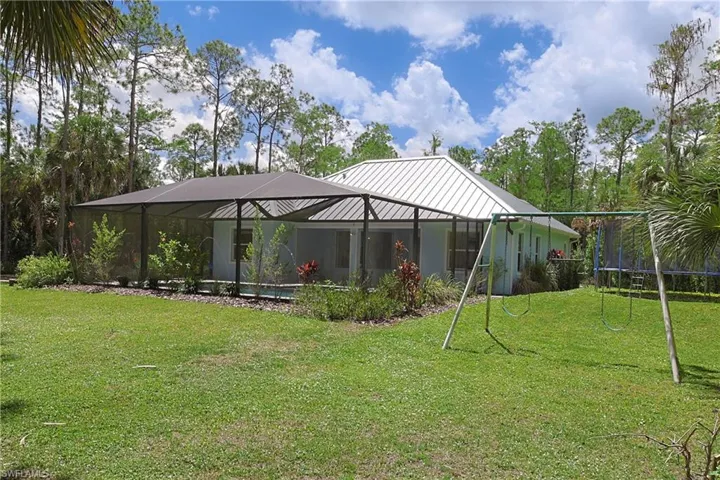 Expansive rear exterior featuring a white metal roof, screened enclosure, and a large grassy yard