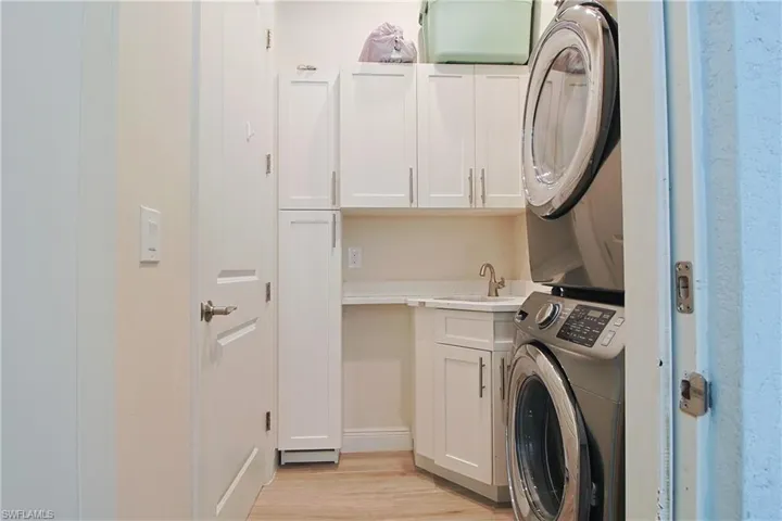 Dedicated laundry area featuring a stacked washer and dryer, white cabinetry with brushed nickel hardware, light-toned countertop with an integrated sink, and wood-finish flooring
