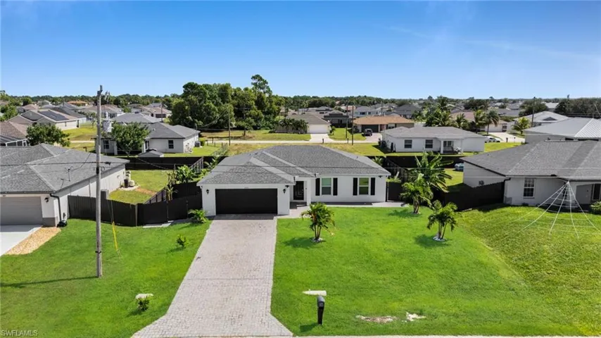 View of front of property with a residential view, decorative driveway, a fenced backyard, and a garage
