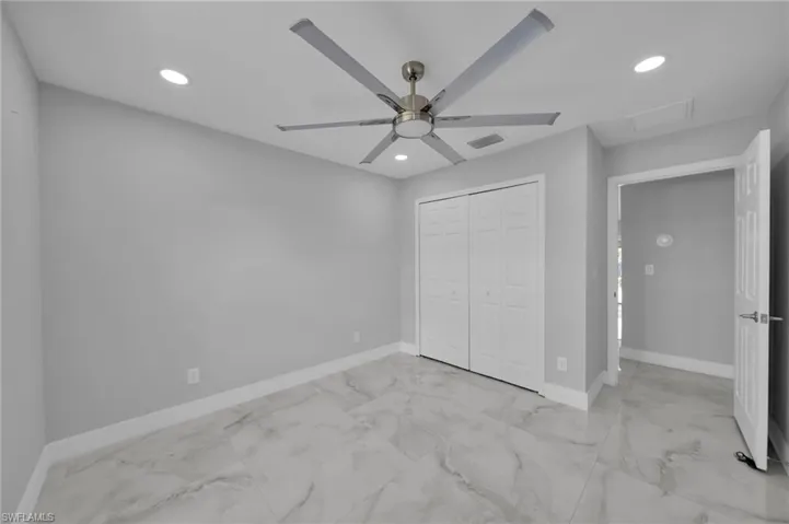 Unfurnished bedroom with light marble finish floors, recessed lighting, attic access, ceiling fan, and a closet