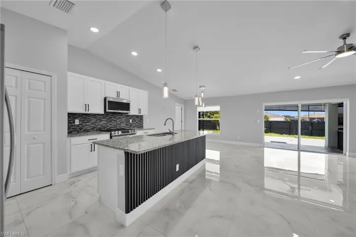 Kitchen with light marble finish floors, pendant lighting, a center island with sink, light stone counters, and tasteful backsplash