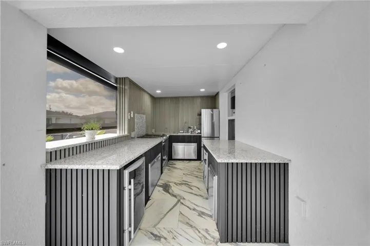Kitchen with light stone counters, light marble finish flooring, recessed lighting, dark cabinetry, and wine cooler