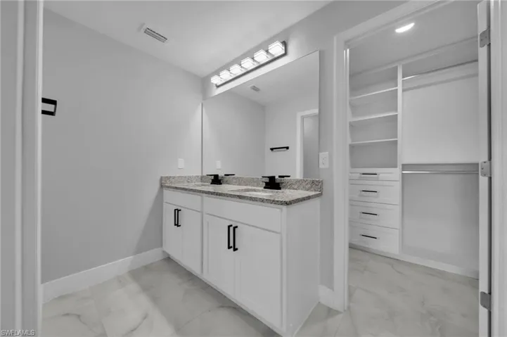 Bathroom featuring double vanity, light marble finish floors, and a spacious closet