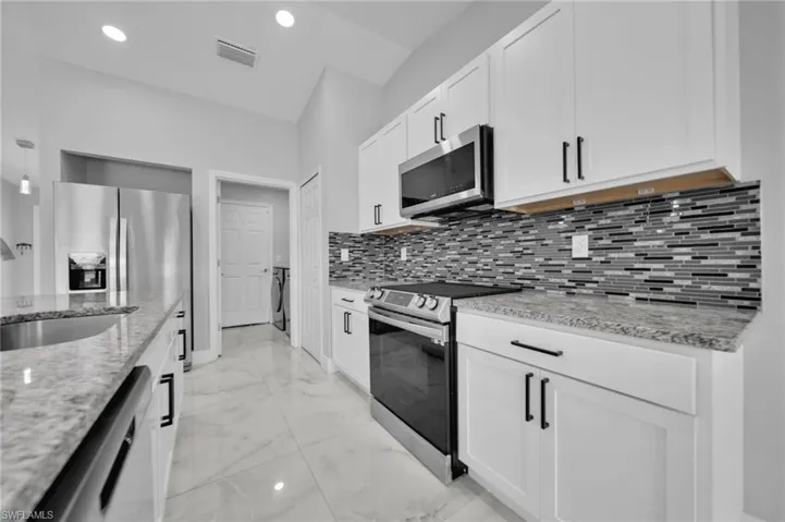 Kitchen with appliances with stainless steel finishes, light stone countertops, light marble finish floors, decorative backsplash, and white cabinets