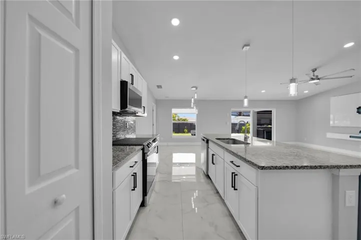 Kitchen with light marble finish floors, hanging light fixtures, white cabinets, light stone countertops, and ceiling fan