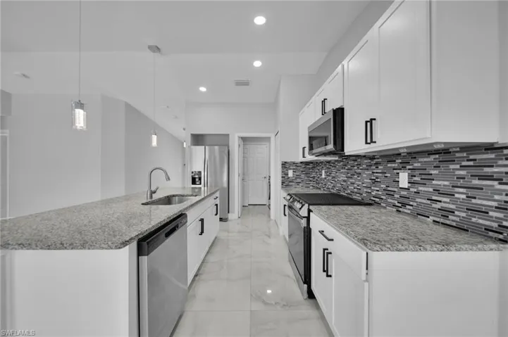 Kitchen with pendant lighting, appliances with stainless steel finishes, an island with sink, light stone counters, and white cabinets