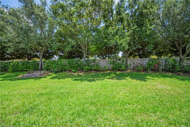 Expansive green lawn framed by mature trees and a privacy hedge