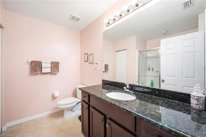 Bathroom featuring a dark-toned vanity with an integrated sink, a speckled countertop, and a large wall-mounted mirror