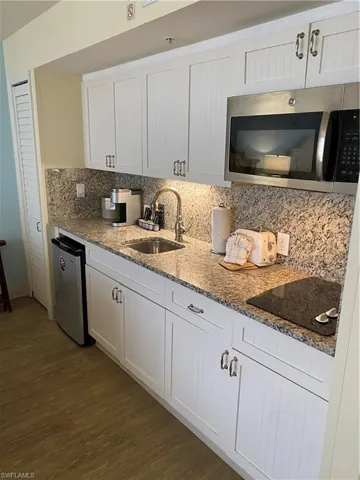 Kitchen with cooktop, sink, backsplash, hardwood / wood-style floors, and white cabinetry