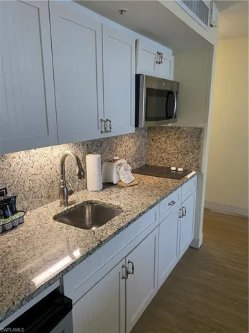 Kitchen with decorative backsplash, light stone counters, white cabinetry, dark wood-type flooring, and sink