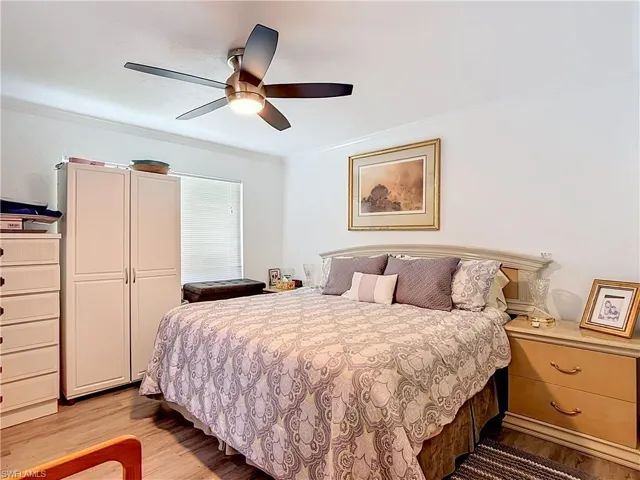 Bedroom featuring wood-finish flooring, a ceiling fan with integrated lighting, crown molding, and a window with horizontal blinds
