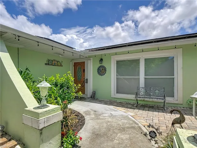Front entry featuring a wood-panel door with oval glass inset, a concrete pathway, and a paver patio area
