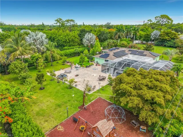 Expansive grounds featuring a screened-in pool enclosure, extensive hardscaping, solar panel array, and a variety of mature tropical landscaping