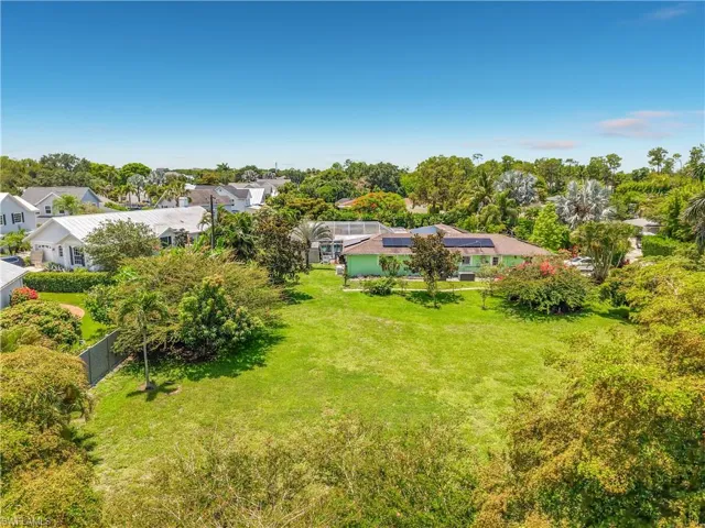 Expansive green lawn with mature trees and a fenced boundary, featuring a residence with a light green exterior, a red roof, and solar panels
